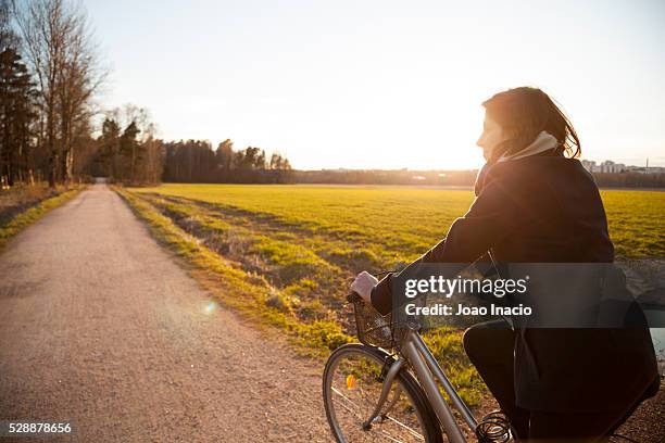 young woman riding bicycle on a rural road at sunset - finland spring stock pictures, royalty-free photos & images