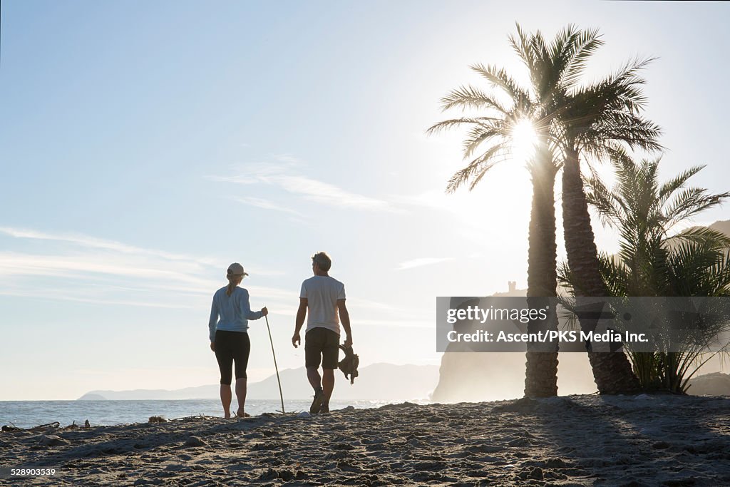 Couple walk along beach, carrying driftwood