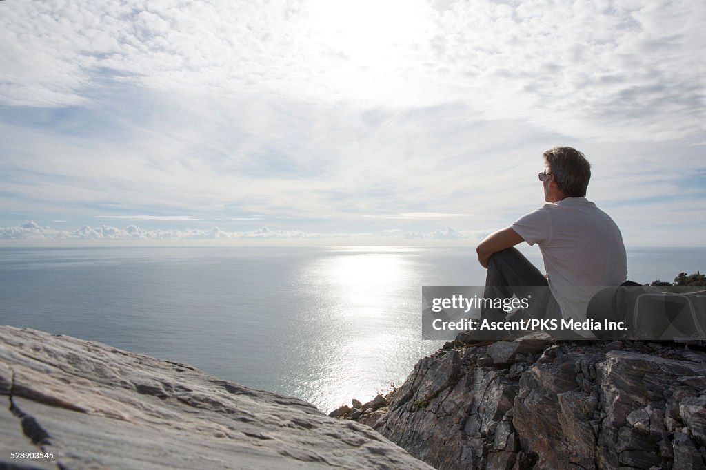Male hiker looks out to sea from rock cliff