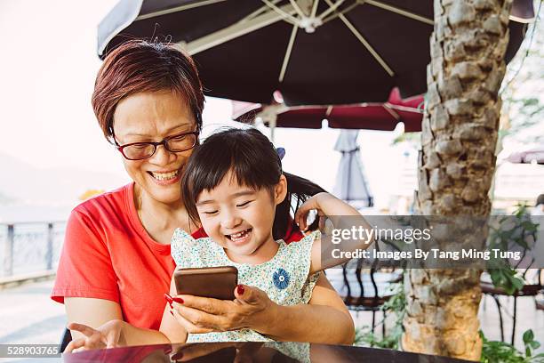 grandma using smartphone with todller in cafe - hong kong grandmother stock pictures, royalty-free photos & images