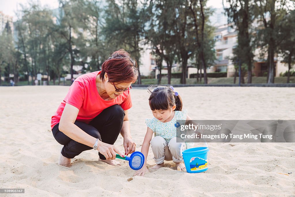 Grandma & toddler playing sand joyfully on beach
