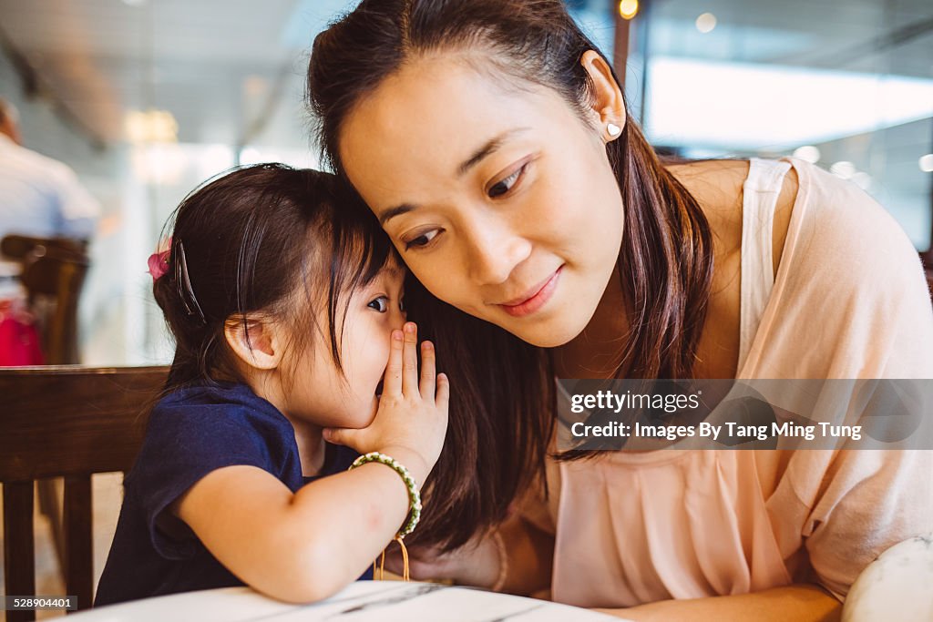 Toddler whispering into mom's ear in cafe