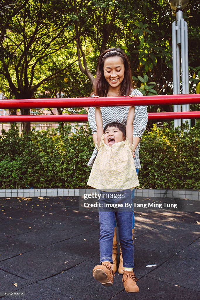 Toddler playing monkey bars with mom in park