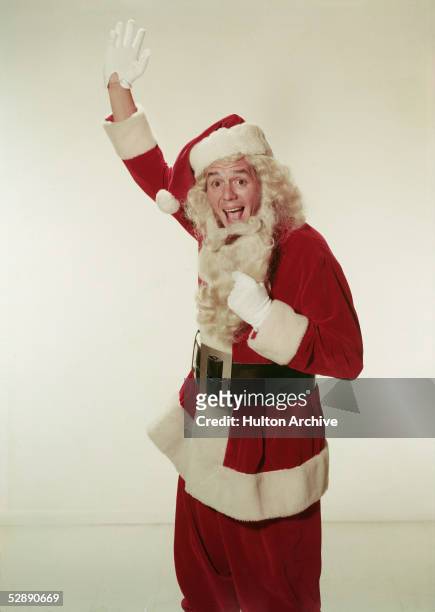 Promotional portrait of Cuban-born musician and actor Desi Arnaz , who waves as he pulls down the beard of his Santa Claus costume, 1950s.