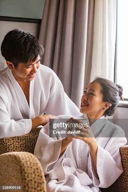 robe wearing young asian couple with a hot drink - asian couple having hi tea stock pictures, royalty-free photos & images