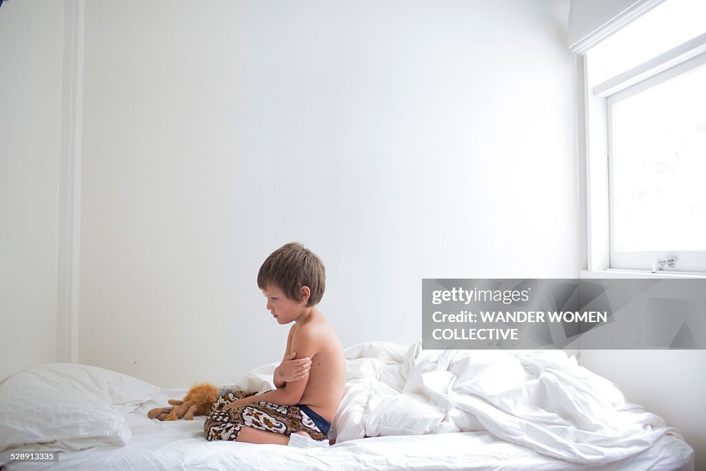 Young boy upset on white bed sheets in room