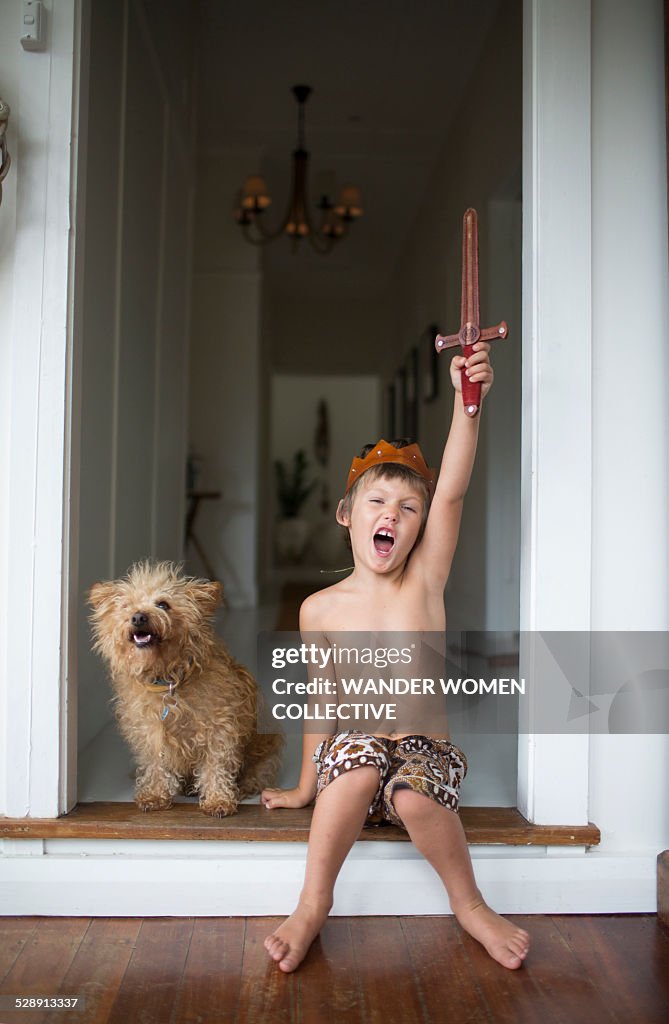 Young boy with sword and crown at home with dog