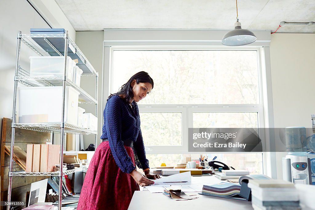 Female office worker looks at plans on a desk.