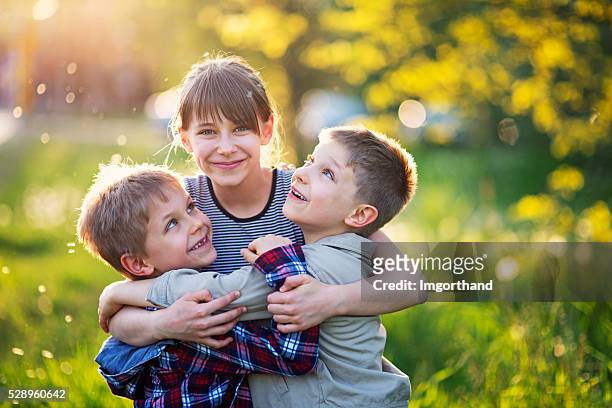 sister embracing younger brothers in dandelion field - sibling stock pictures, royalty-free photos & images