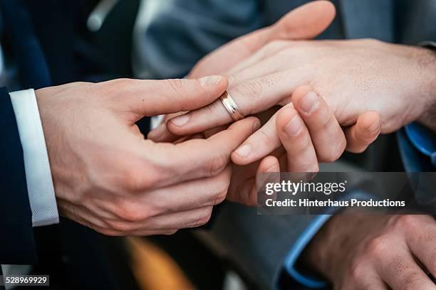 gay wedding groom placing ring on husband - gay stockfoto's en -beelden