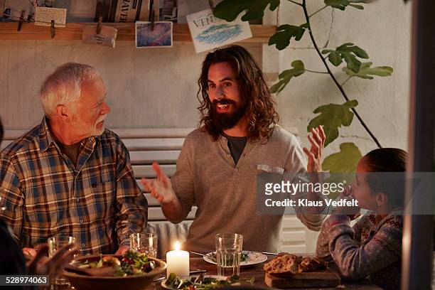 man telling a story at family dinner in garden hou - candle light dinner stock pictures, royalty-free photos & images