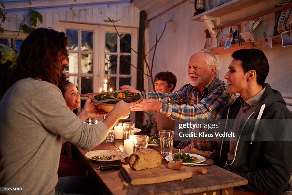 Senior man passing bowl of salad to son