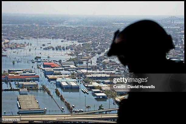 Army loadmaster sits at the open back of a search and rescue chinook helicopter, while flying over a flooded New Orleans.