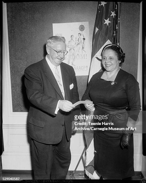 Mayor Thomas J Gallagher exchanging check with Wilhelmina Byrd Brown, New York', Pittsburgh, Pennsylvania, circa 1959. Behind them is a poster...