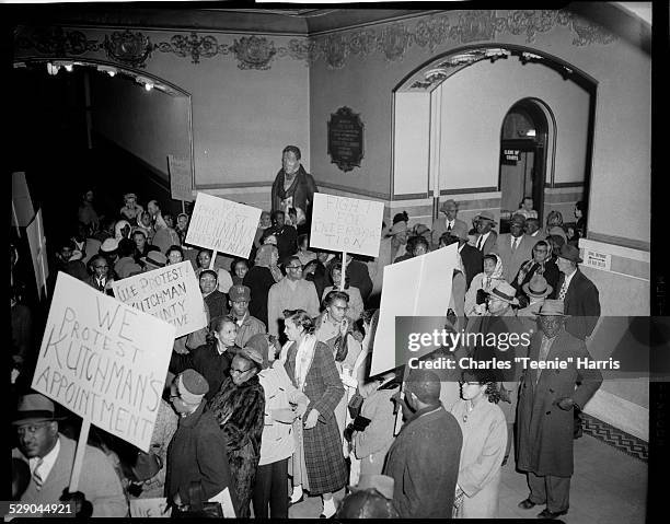 Protesters inside courthouse carrying placards inscribed 'We Protest Kutchman's Appointment,' with Clerk of County Courts, Civil Defense, and Air...