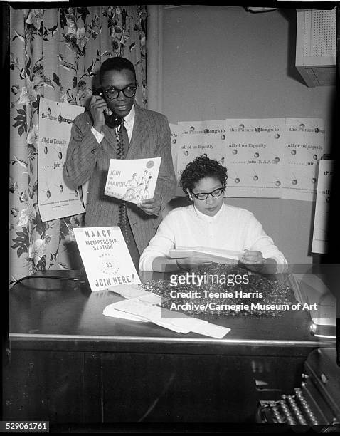 Man holding telephone receiver and document inscribed 'Join the March to Freedom,' and woman seated at desk, with sign reading 'NAACP Membership...