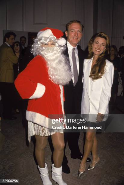 American actress Angie Dickinson wears a Santa Claus costume as she poses with American actor James Keach and British actress Jane Seymour at an...