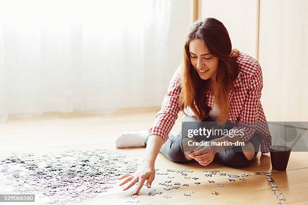 woman arranging jigsaw puzzle at home - jigsaw puzzle stock pictures, royalty-free photos & images