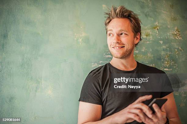 man standing at wall, writting message and looking away - holding smart phone stock pictures, royalty-free photos & images