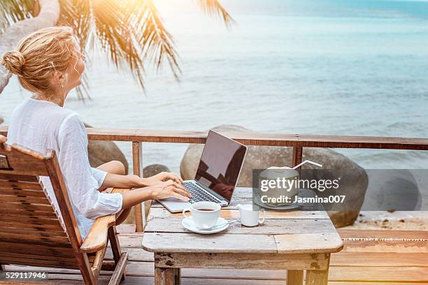 young woman working on laptop with coffee and young coconut - exoticism stock pictures, royalty-free photos & images