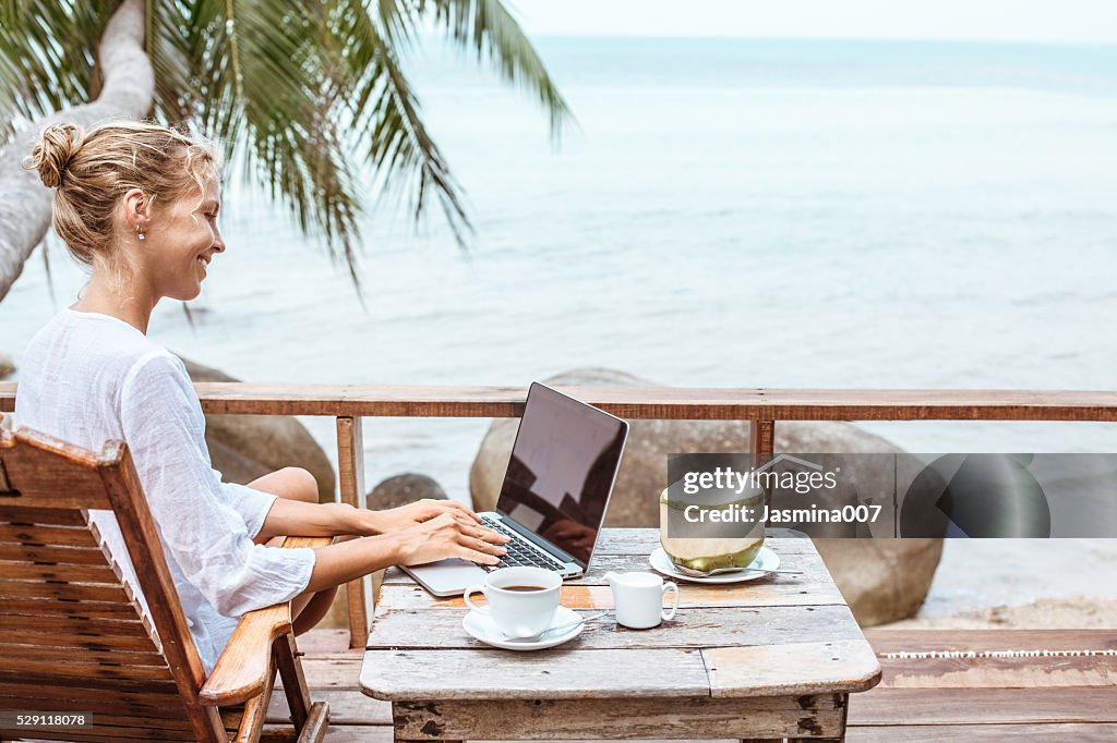 Young woman working on laptop with coffee and young coconut