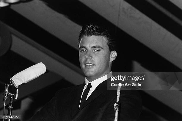Rick Nelson, standing under a striped awning, with microphones; circa 1970; New York.
