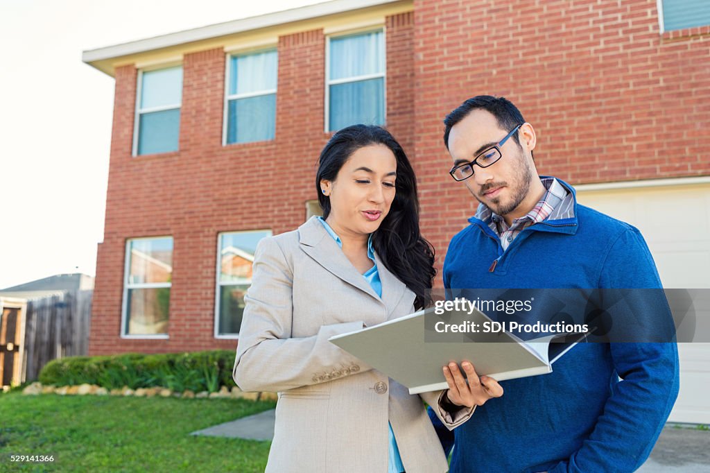 Real Estate Agent discusses paperwork with client in front of new home