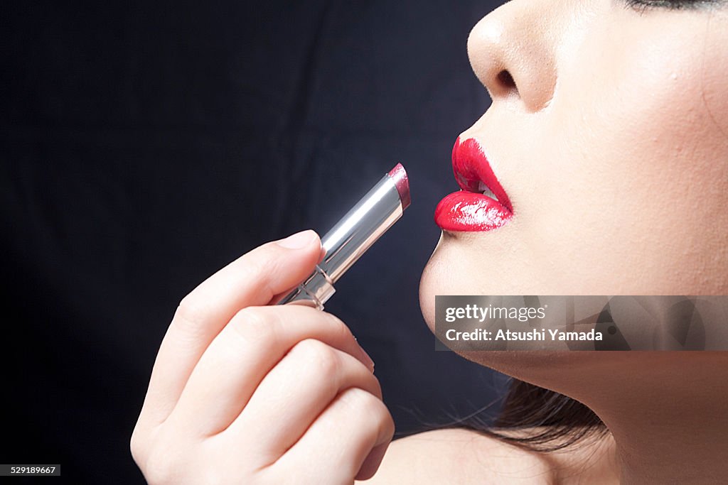 Asian woman putting red lipstick, hand close up