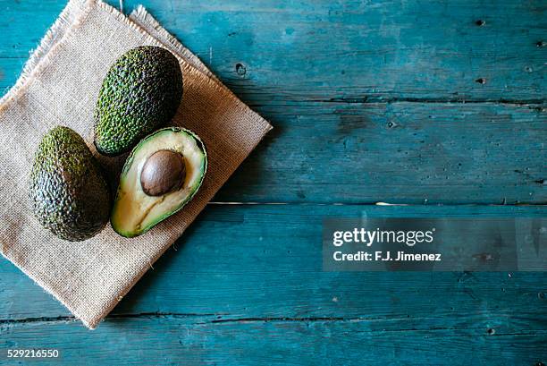 whole and halved avocado on wooden table - avocado stock-fotos und bilder