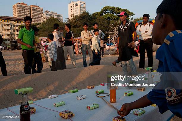 Boys attempt to win bars of soap by throwing rings on bottles of soda pop. Locals and tourists visit Chaowpatty Beach in Mumbai. Traditionally the...