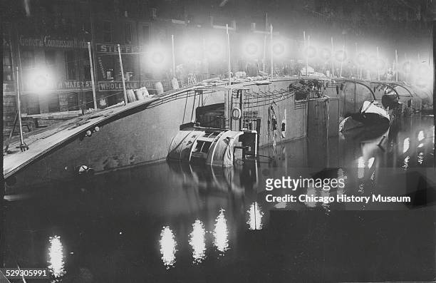 Overturned Eastland ship in the Chicago River at night, Chicago, Illinois, 1915. Powerful electric lights aid workers and rescuers.