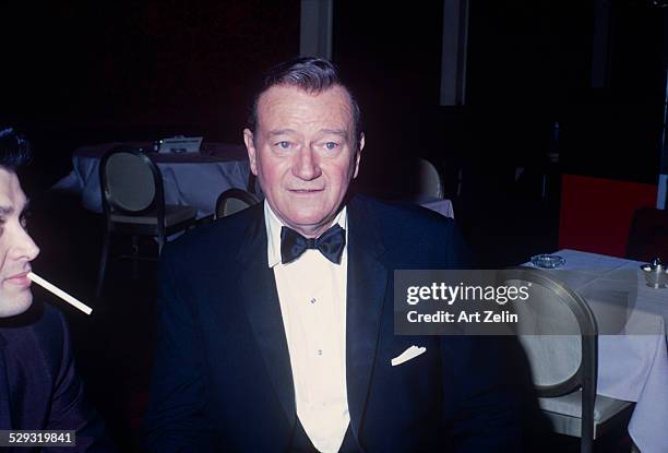 John Wayne in a tux at a table; circa 1970; New York.