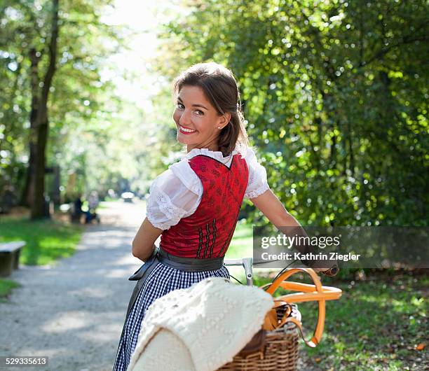 woman wearing dirndl dress, pushing her bicycle - traditionelle kleidung stock-fotos und bilder