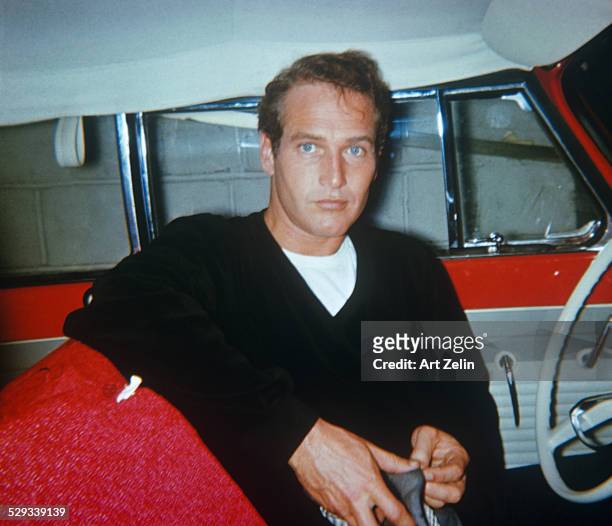 Paul Newman in the 1950's, sitting in a red car with white interior. The photograph was taken with a star flash camera. The photographer was walking...