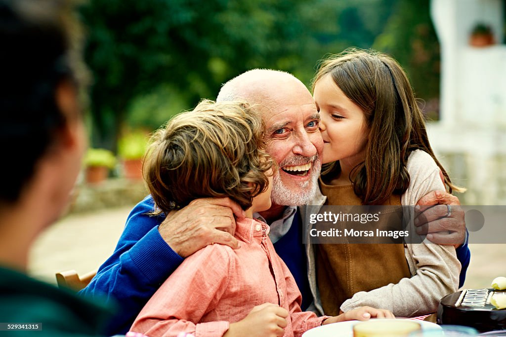 Children kissing grandfather at yard