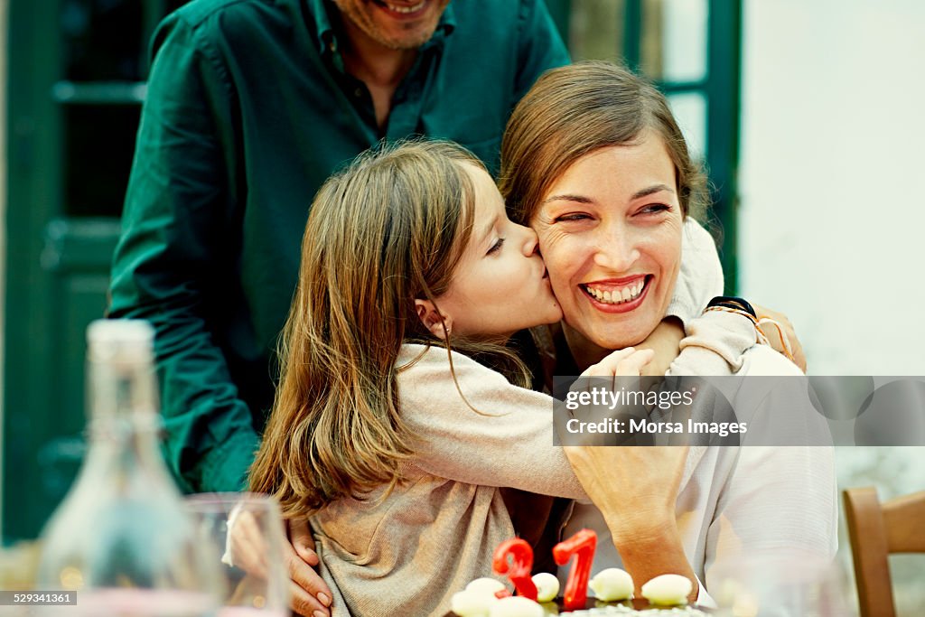 Girl kissing mother while celebrating birthday