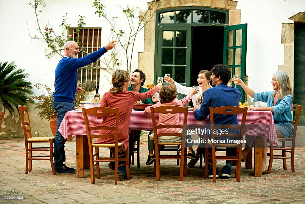 Senior man raising toast to family at meal table