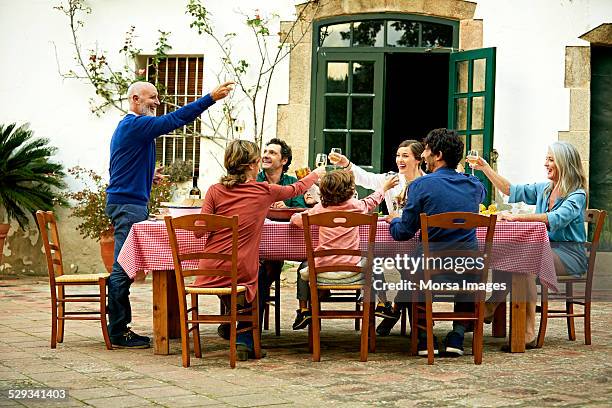 senior man raising toast to family at meal table - standing table outside stock pictures, royalty-free photos & images