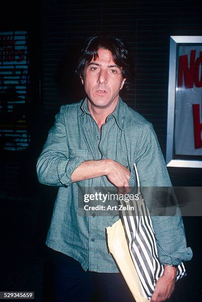 Dustin Hoffman with a shopping bag wearing a gray checked shirt; circa 1970; New York.