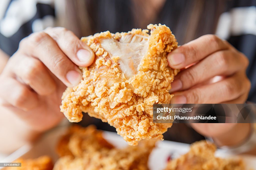 Hand holding Fried chicken and eating in the restaurant