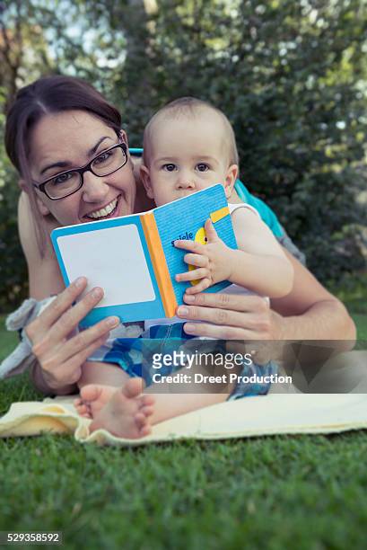 mother and baby boy holding a picture book and laughing in lawn, munich, bavaria, germany - need reading glasses stock pictures, royalty-free photos & images