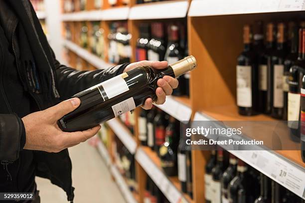 customer reading label on red wine bottle in a supermarket, munich, bavaria, germany - liquor store stock pictures, royalty-free photos & images