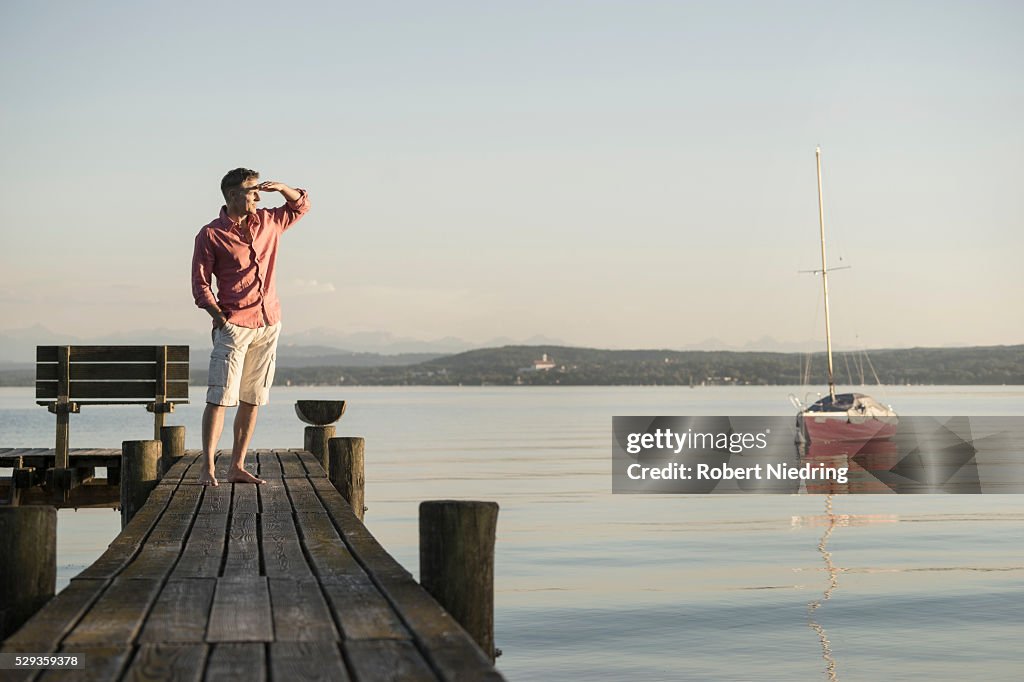 Mature man standing on wooden pier and looking at distance, Bavaria, Germany,