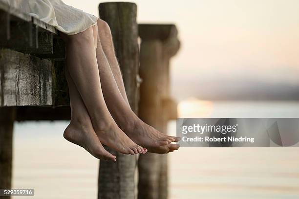 couple legs dangling on pier, bavaria, germany - pier sunset imagens e fotografias de stock