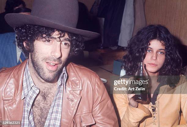 Elliott Gould and Jennifer Bogart, sitting at a table in a diner wearing leather jackets; circa 1970; New York.