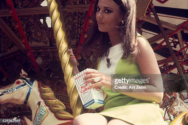 Natalie Wood in California sitting on a merry go round holding a box of popcorn; circa 1970; New York.