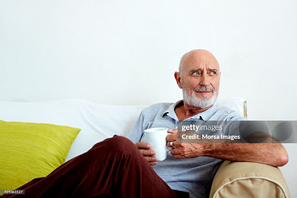Thoughtful senior man holding coffee mug on sofa
