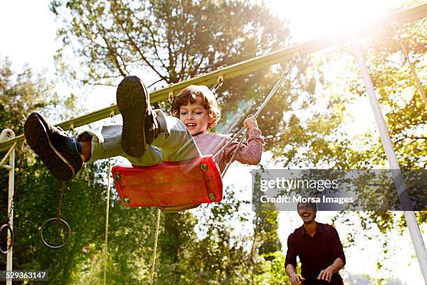 father pushing son on swing in park - parents and children enjoying park photos et images de collection