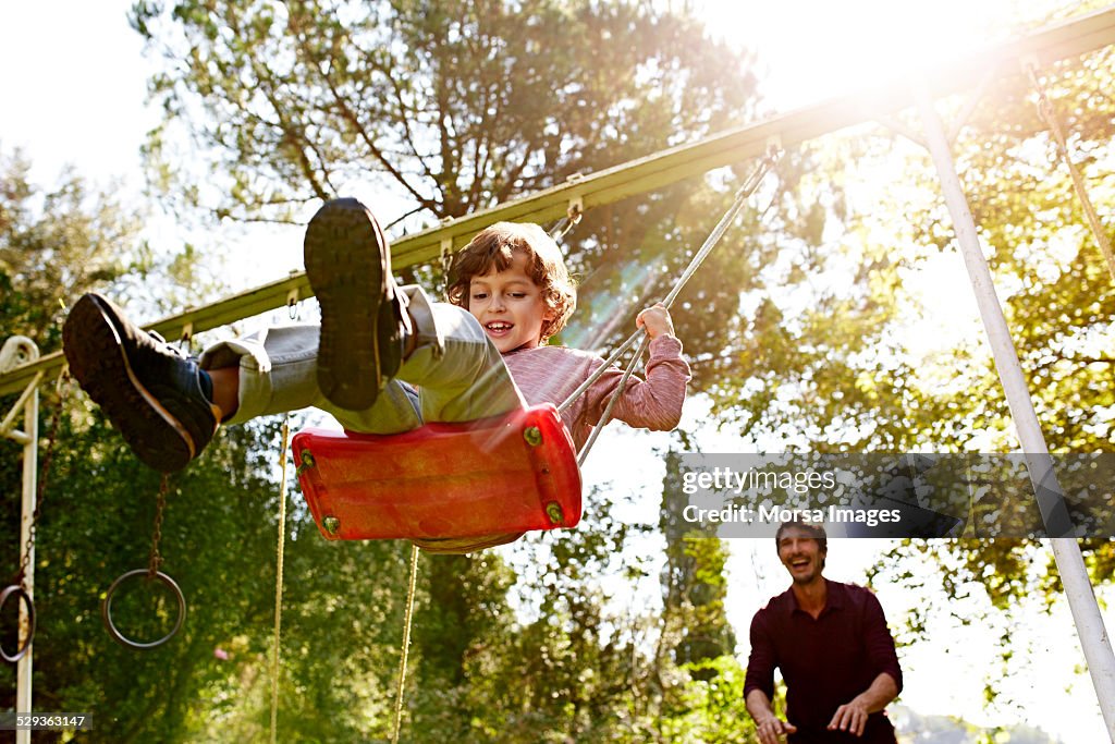 Father pushing son on swing in park