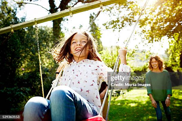 mother pushing daughter on swing in park - family outside stock pictures, royalty-free photos & images